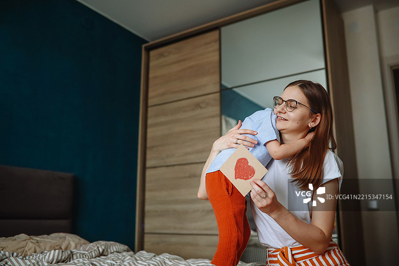 孩子的温柔与爱：小男孩在温馨的家中给妈妈一个心形礼物图片素材