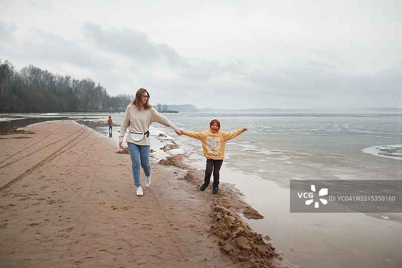 雾蒙蒙的早晨：母女俩手牵手走在冰冻湖边图片素材