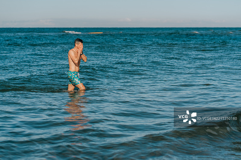 男子走入寒冷的冬季海水中，捂住脸部图片素材