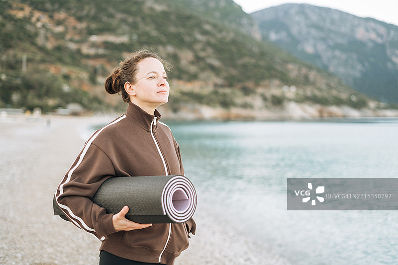 美丽的年轻棕发中年女性在清晨海边练习瑜伽，关注身心健康图片素材