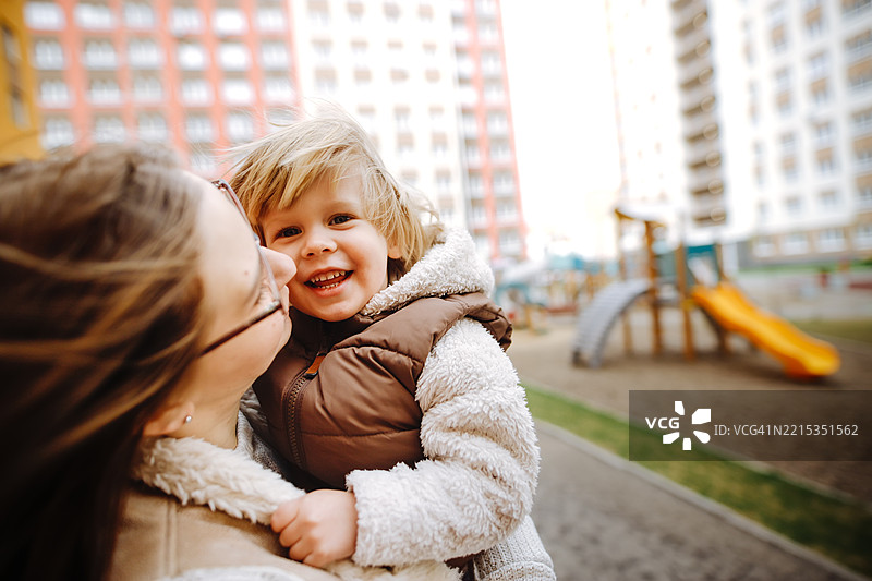 年轻母亲与她的儿子在新建的设施齐全的社区游乐场玩耍。图片素材