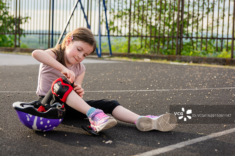 一个女孩在运动场上坐着时戴上护膝。图片素材