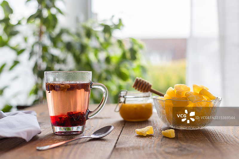 木桌上冒着热气的草本茶，配有蜂蜜和蜜饯姜片图片素材