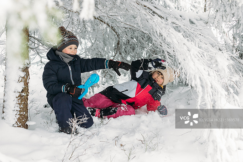 两个快乐的孩子在冬季假期里，在一棵被雪覆盖的树下玩耍，制作雪团。图片素材