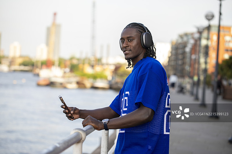 一位年轻男子在黄昏时分坐在河边戴着耳机听音乐图片素材