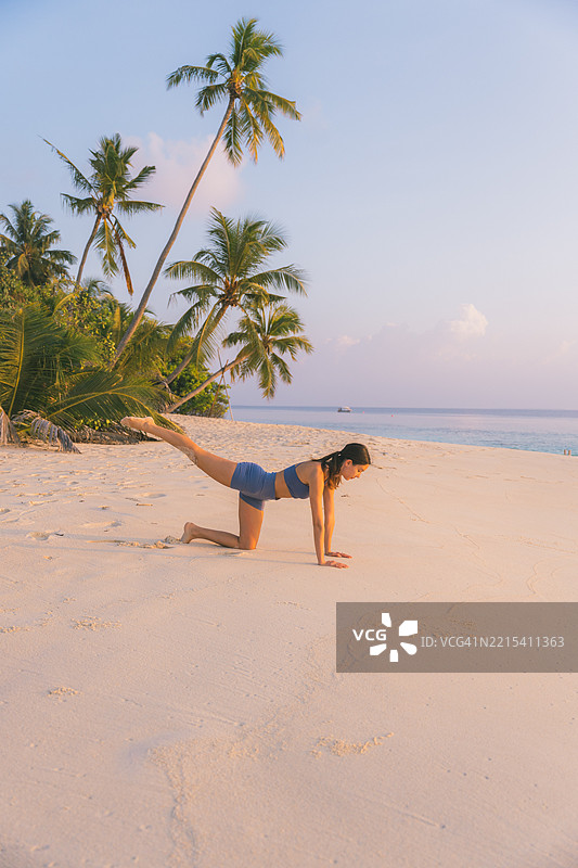 年轻女性在日出时分的海滩上做瑜伽动作图片素材