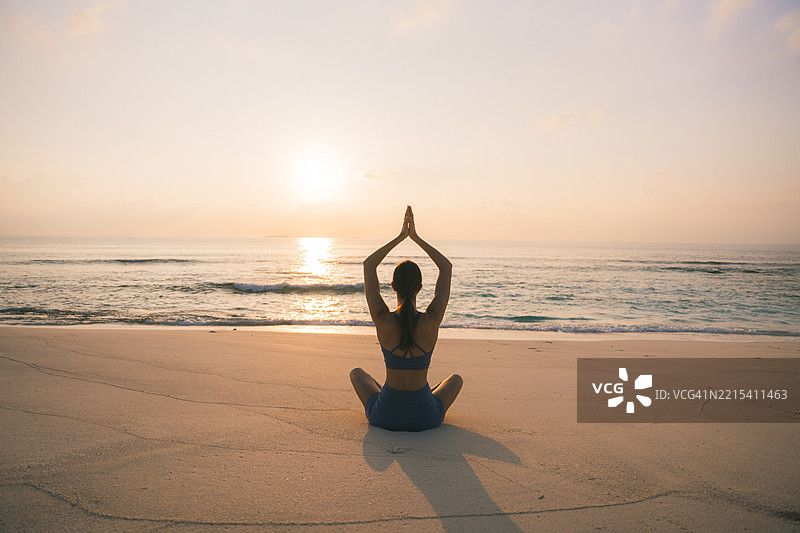 年轻女性在日出时分的海滩上做瑜伽动作图片素材