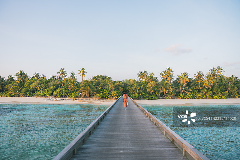 年轻女性走在热带泻湖上的木栈道上图片素材