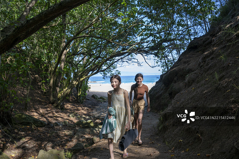 姐妹们在森林小径上漫步，远处是海滩和海洋。图片素材