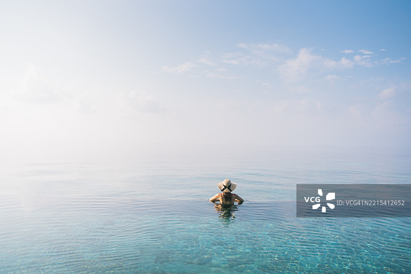 年轻女性在无边泳池边放松。图片素材