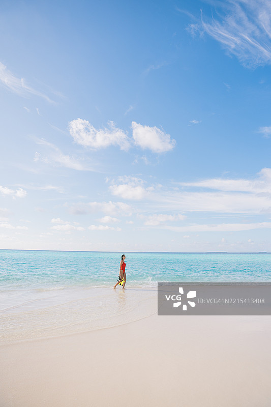 年轻女性穿着潜水装备在海滩浅水区行走图片素材