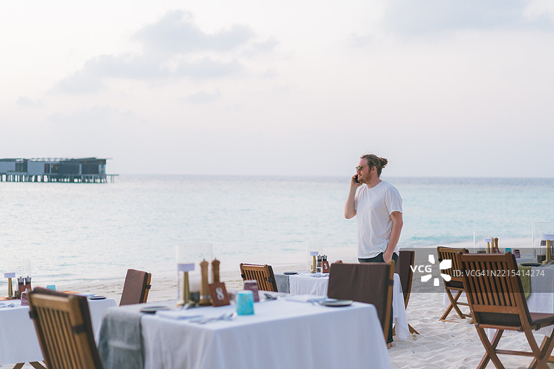 年轻男子在海滩餐厅的日落时分打电话图片素材