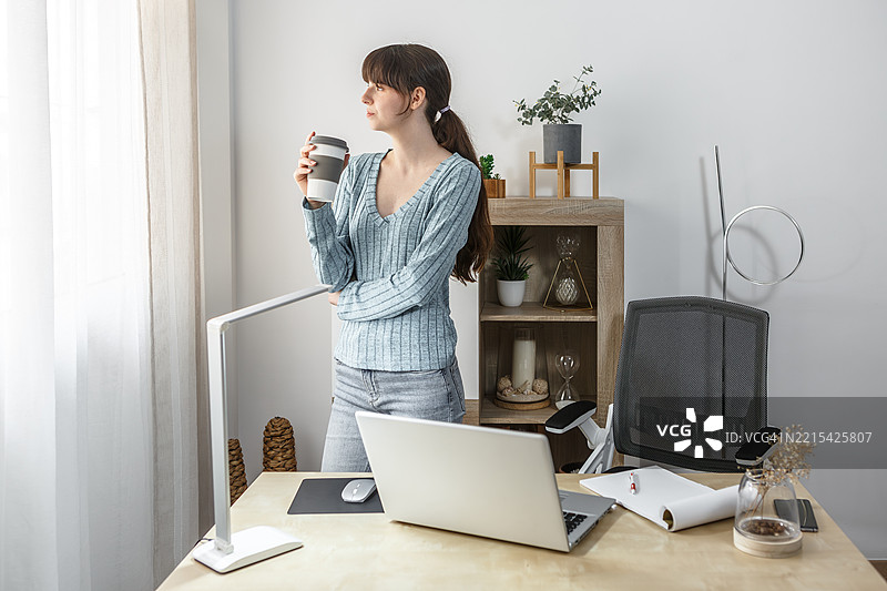 年轻女性在时尚的家庭办公室空间中享受咖啡图片素材