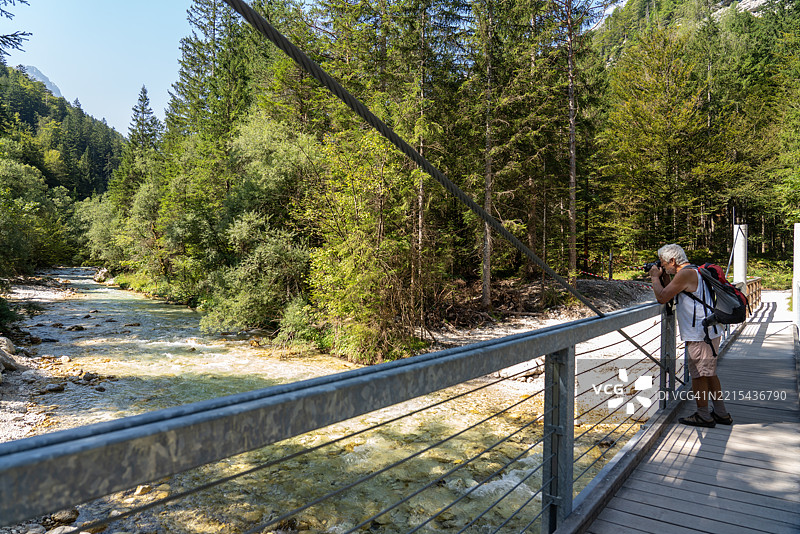 在斯洛文尼亚的桥上，男人们在徒步旅行并拍照，背景是山间河流。图片素材