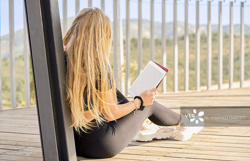 年轻女性坐在木质露台上使用一台空白屏幕的平板电脑图片素材