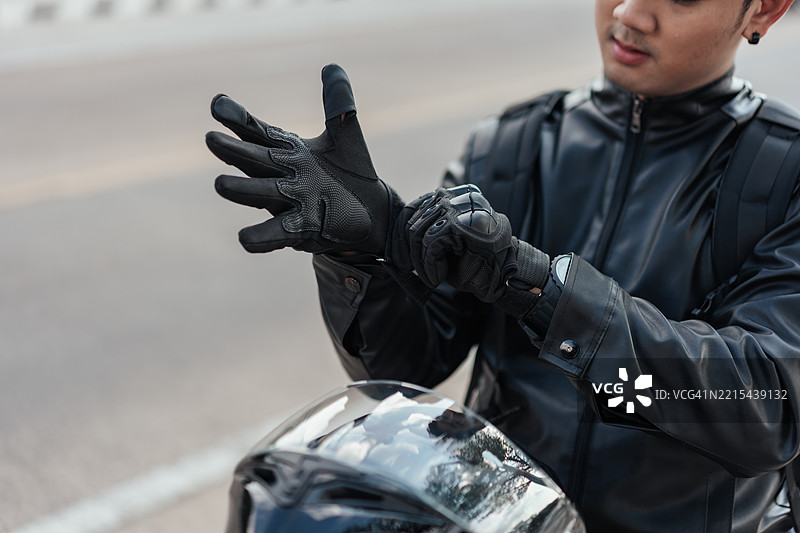 亚洲男性摩托车手在骑行前戴上安全手套。特写镜头展示了负责任的骑行行为、保护装备以及现代城市环境中的自然光线。图片素材