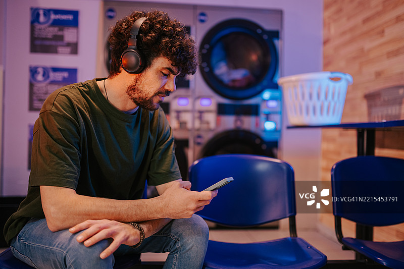 年轻男子在自助洗衣店等待时听音乐图片素材