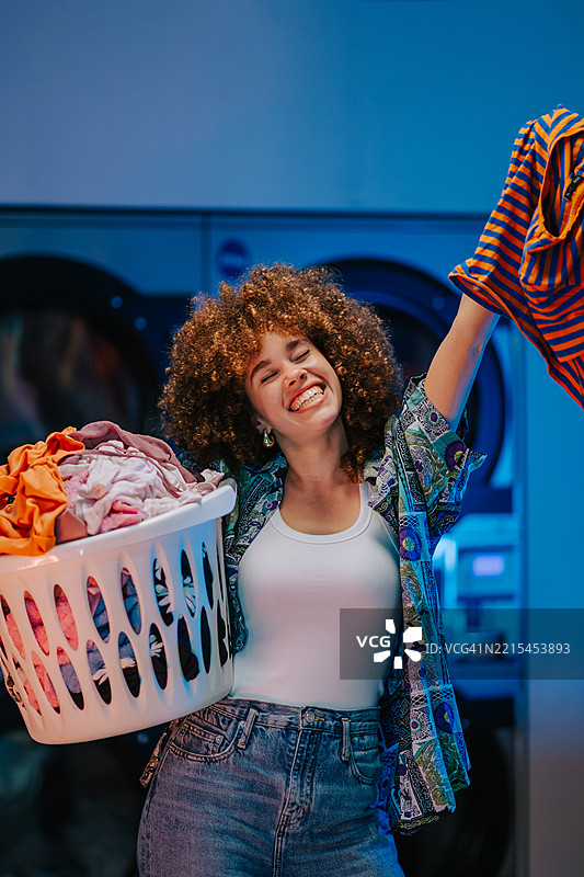年轻女性在自助洗衣店里抱着洗衣篮和干净的衣物图片素材
