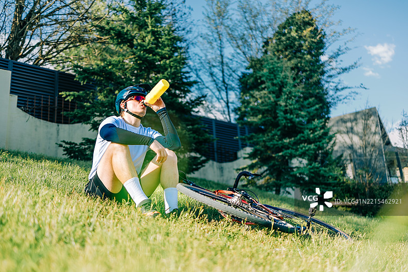 骑自行车的人在草坡上休息时喝水瓶里的水图片素材