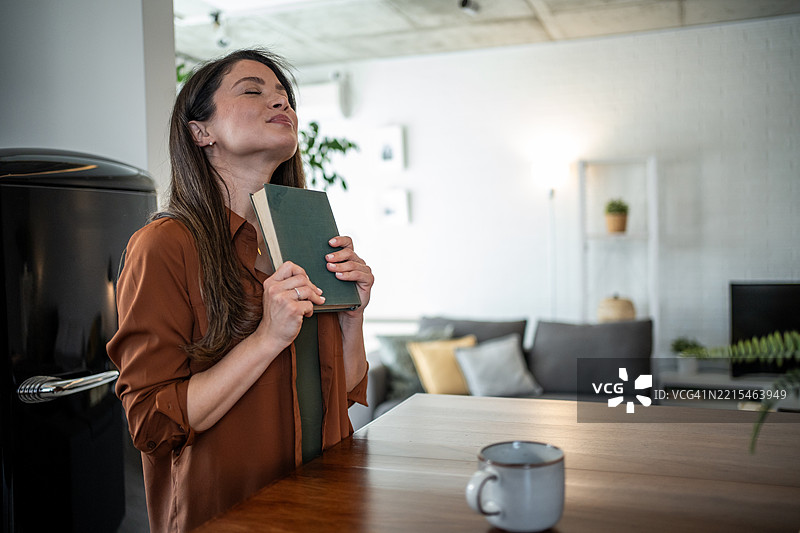 女人微笑着闭上眼睛，抱着一本书在胸前。图片素材