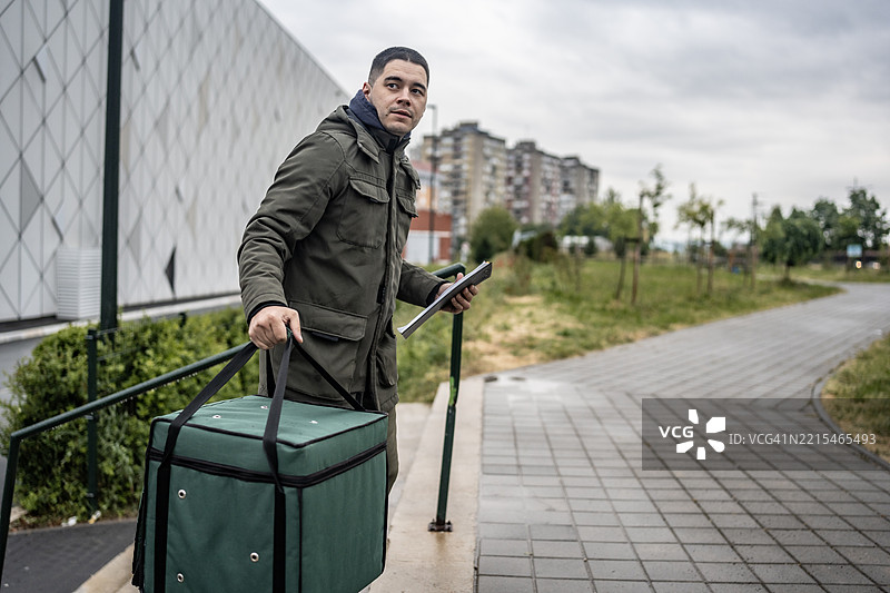 户外城市区域，一名送货员携带保温袋并使用平板电脑图片素材