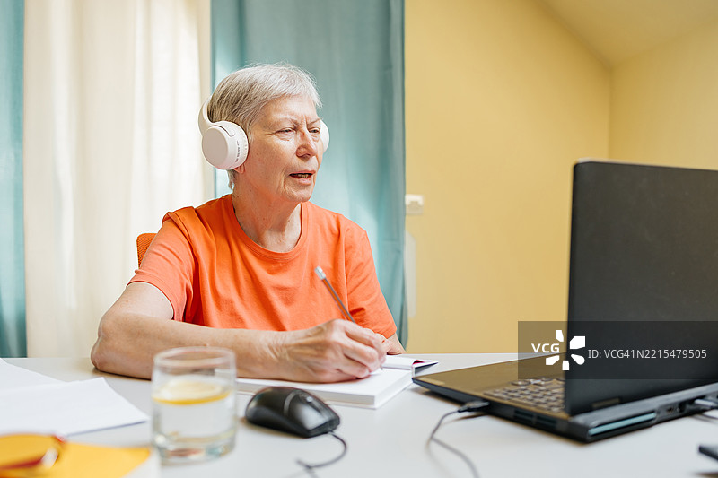 快乐的老年女性戴着耳机在笔记本电脑上学习在线课程并进行视频聊天图片素材