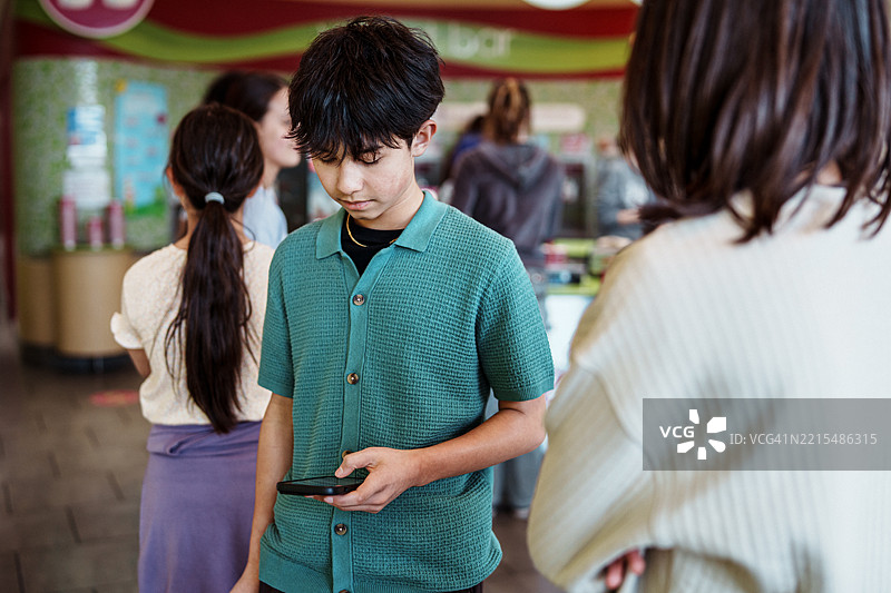 少年在冰淇淋店排队时使用智能手机图片素材