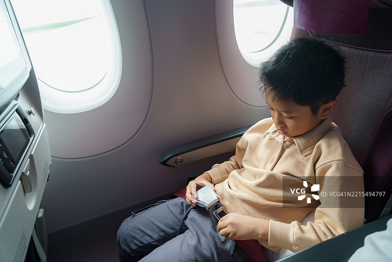 亚洲男孩在飞机座位上系安全带图片素材