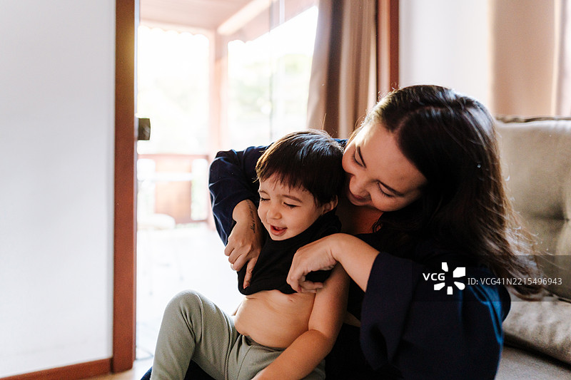 母亲在地板上给儿子穿衬衫图片素材