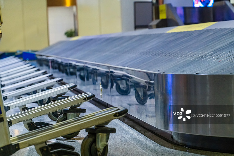 机场航站楼内的空行李传送带，前景中排成一排的行李推车在等待乘客。图片素材