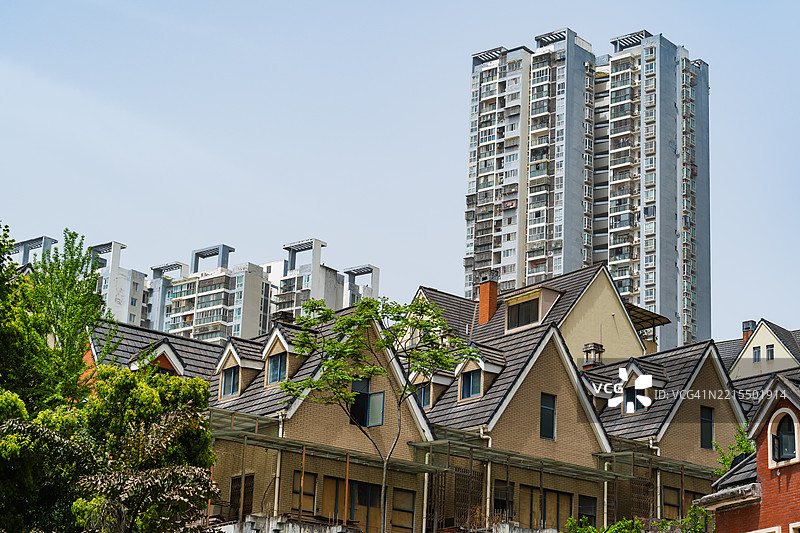 高层公寓大楼在传统郊区风格住宅后面拔地而起，展现了城市密度与居住生活的融合。图片素材