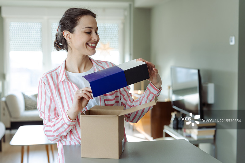 微笑的女性打开包裹，发现里面是蓝色礼盒的内容图片素材