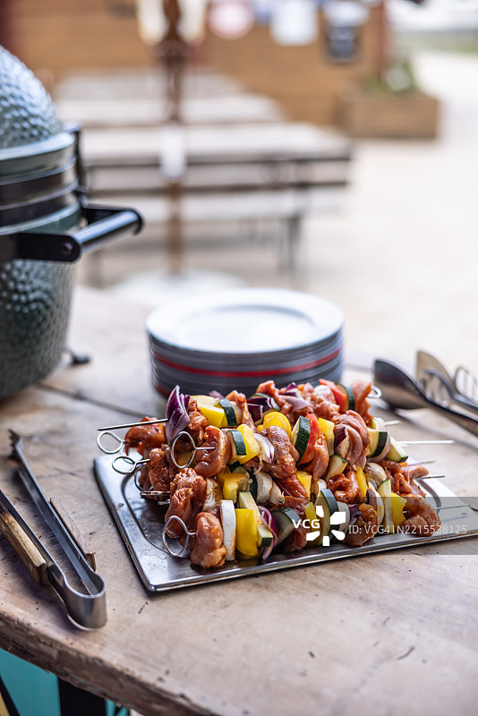 几串鸡肉串和蔬菜放在托盘上，准备在花园烧烤架上烤制。图片素材