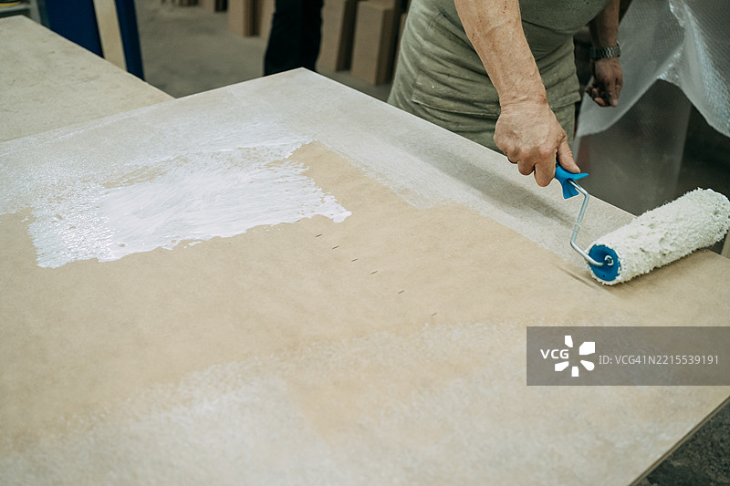 木匠在工作坊里用油漆滚筒在木板上涂胶。图片素材