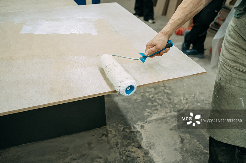 木匠在工作室里用滚筒给木板涂底漆图片素材