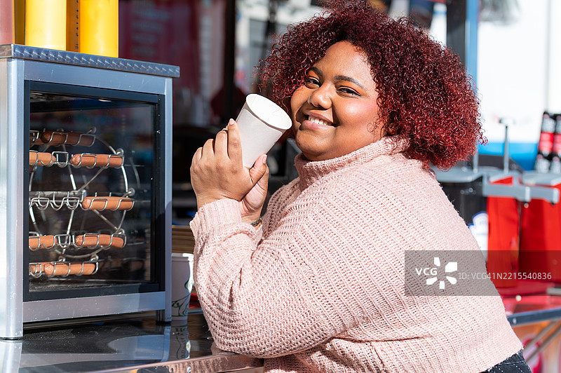 年轻女性在游乐场的食品摊位享受饮品图片素材