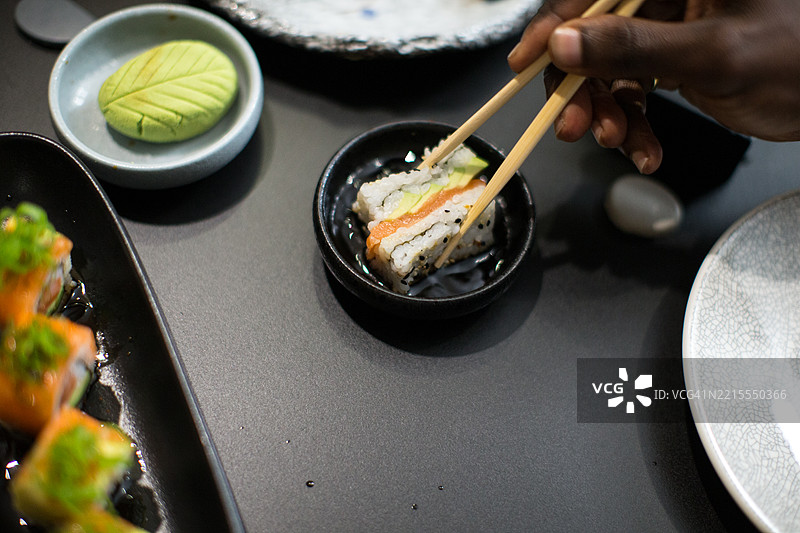 年轻男子用木筷子将寿司蘸入酱油中图片素材