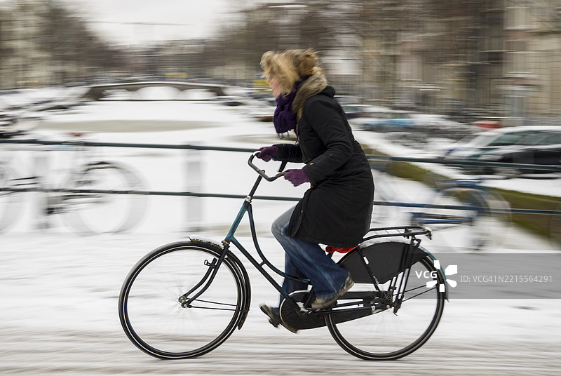 勇敢地面对冬季寒冷，一名骑自行车的人在阿姆斯特丹的雪街上骑行。图片素材
