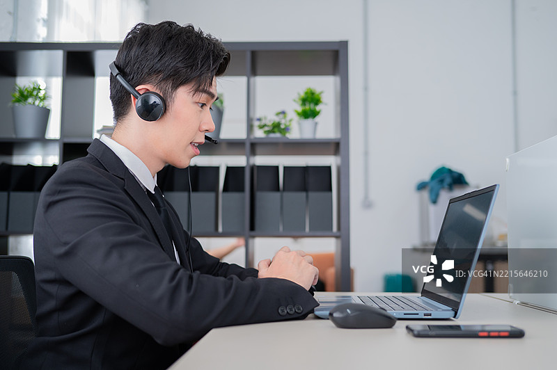 侧面角度照片，亚洲年轻商人戴着耳机使用笔记本电脑工作图片素材