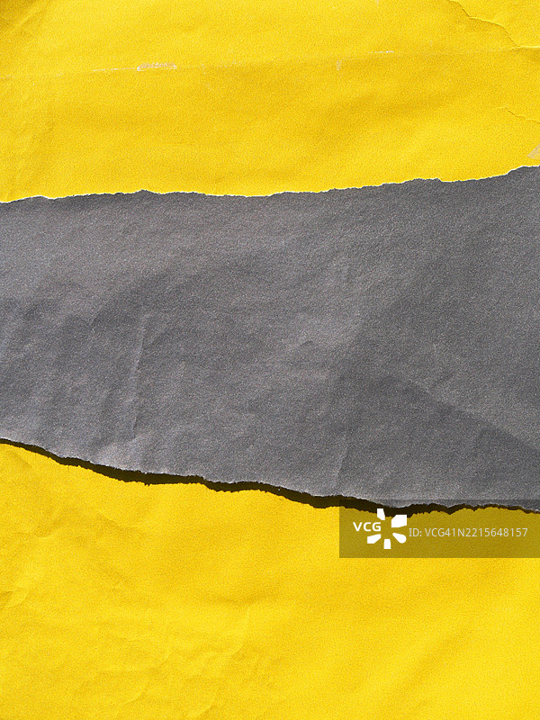 撕裂的灰色纸张覆盖在揉皱的、有纹理的黄色纸张上。阳光。自然色彩和光泽。全画幅 4:3，法国巴黎。图片素材