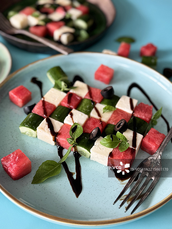 蓝色盘子上的午餐图像 / 西瓜希腊沙拉，配有羊奶酪、黄瓜、罗勒、橄榄油调料和切丁的哈密瓜块图片素材