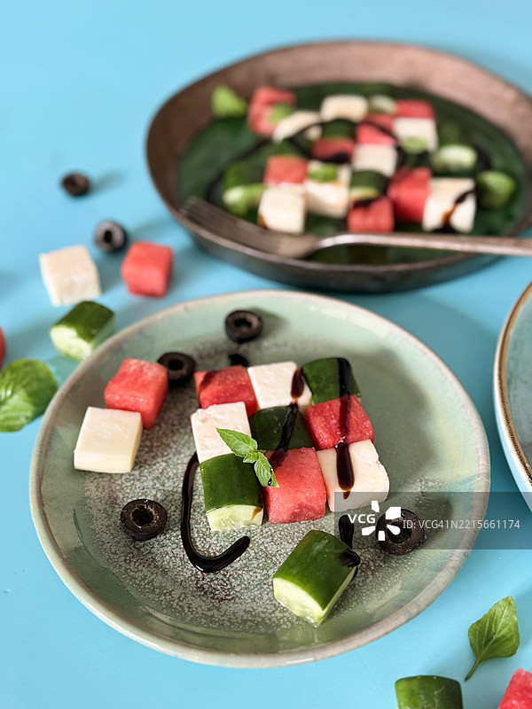 清爽的夏季午餐：蓝色盘子上的西瓜希腊沙拉，配有羊奶酪、黄瓜、罗勒和橄榄油 / 健康的切丁甜瓜菜肴图片素材