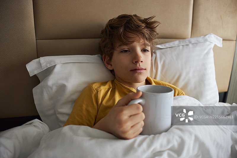 疲惫的男孩在床上喝茶图片素材