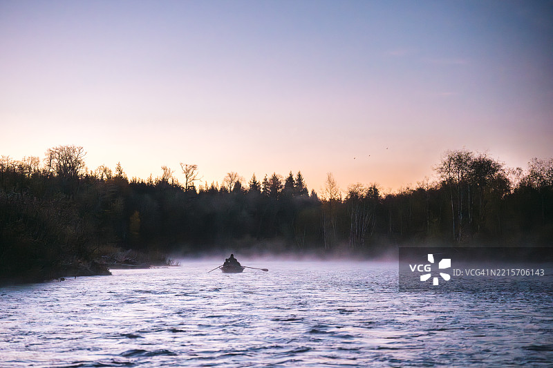 黄昏时分，一对情侣在钓鱼船上顺流而下图片素材