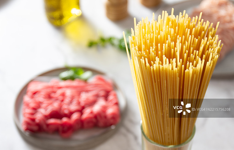 干意大利面整齐地放在一个罐子里，旁边有新鲜的肉和香草，准备在厨房中烹饪图片素材
