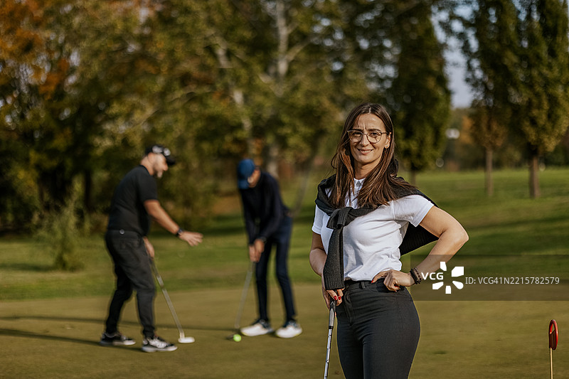高尔夫教练在郁郁葱葱的球场上教学生们。图片素材