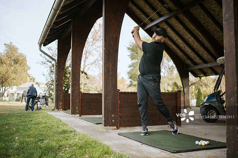 男子在户外练习场练习高尔夫挥杆图片素材