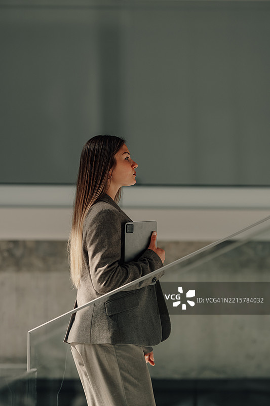 年轻女商人手持平板电脑在现代办公室的楼梯上走动图片素材