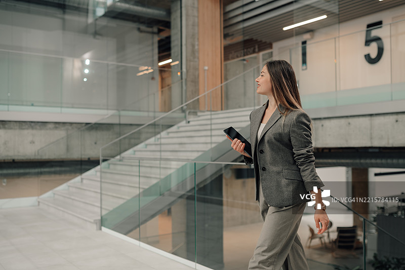 女商人在现代办公大楼中走动，手持平板电脑图片素材