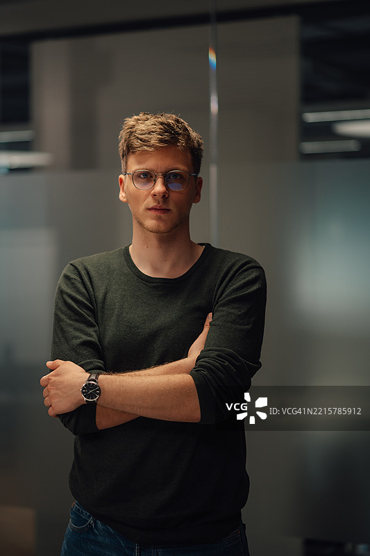 自信的年轻商人在办公室摆姿势，双臂交叉。图片素材